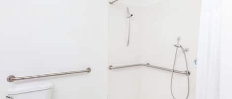 Un baño con inodoro, ducha con cabezal de ducha manual y barras de apoyo.