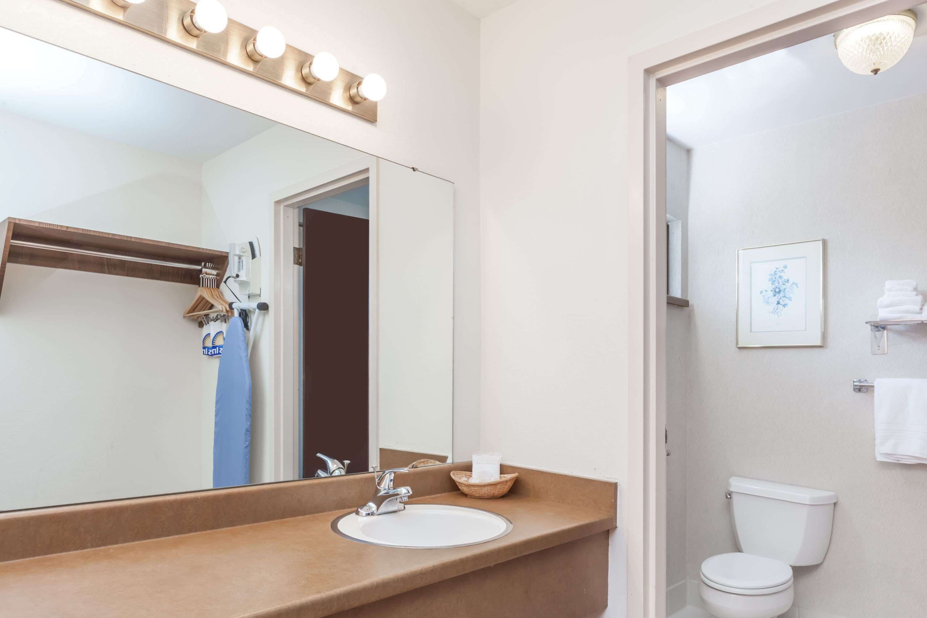 A bathroom with a vanity, sink, mirror, and toilet.