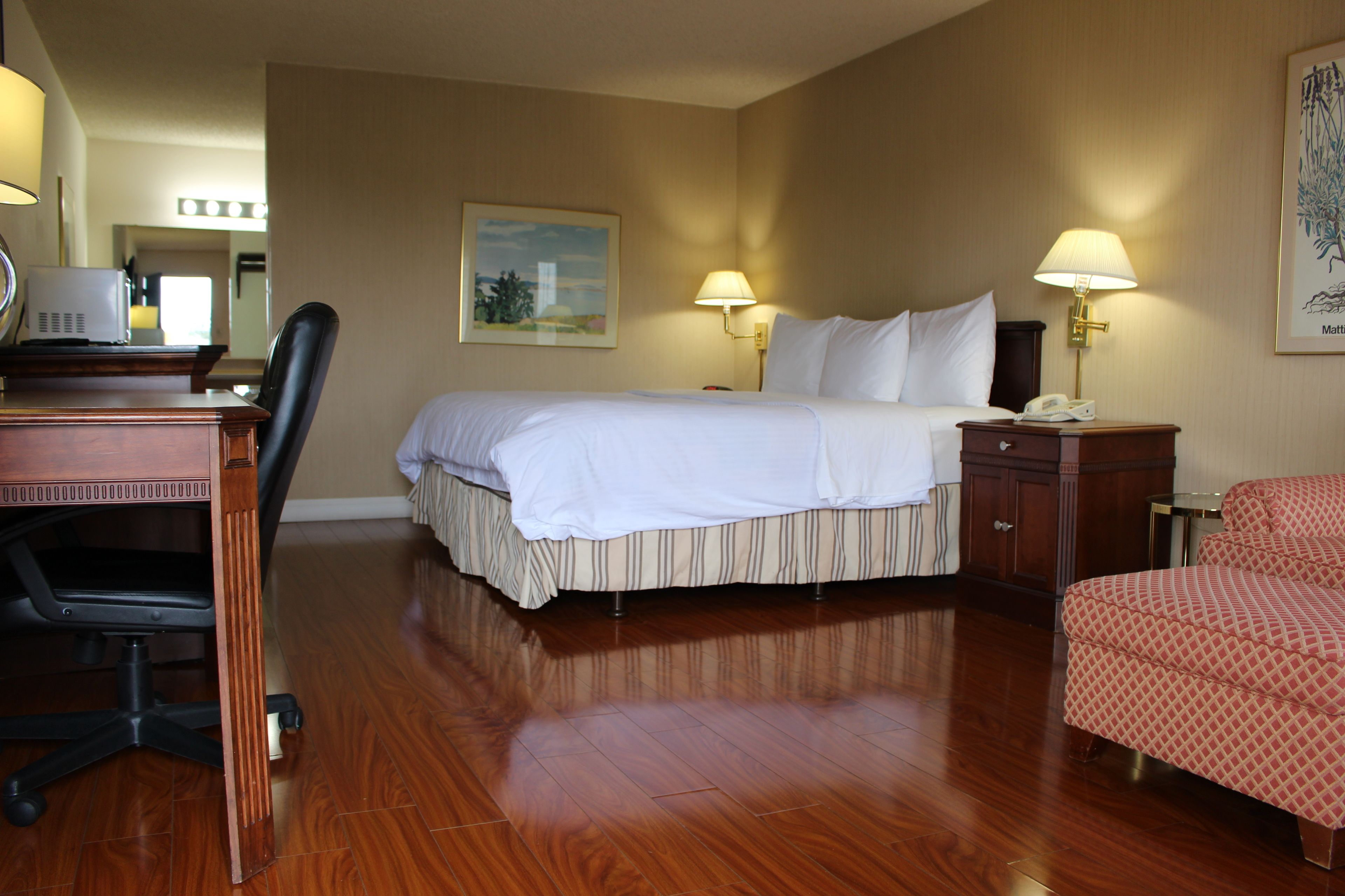 A hotel room with a bed, desk, chair, and lamps.