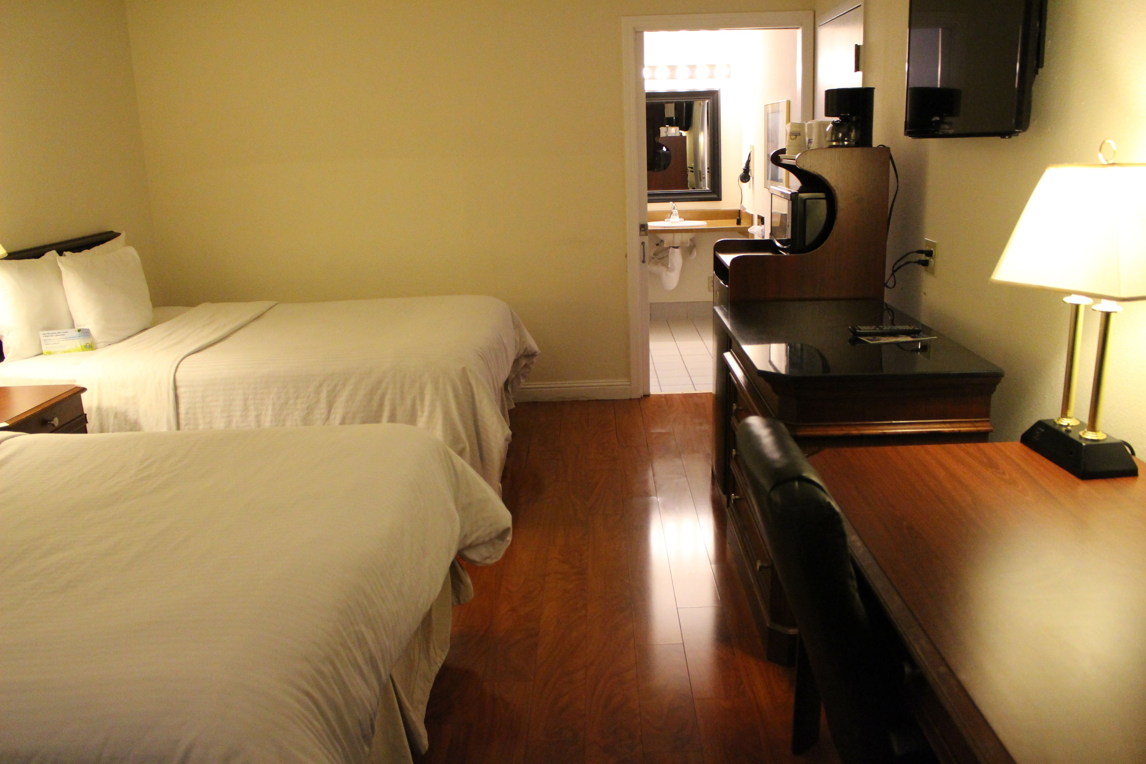 A hotel room with two beds, a desk, a chair, a TV, and a lamp.