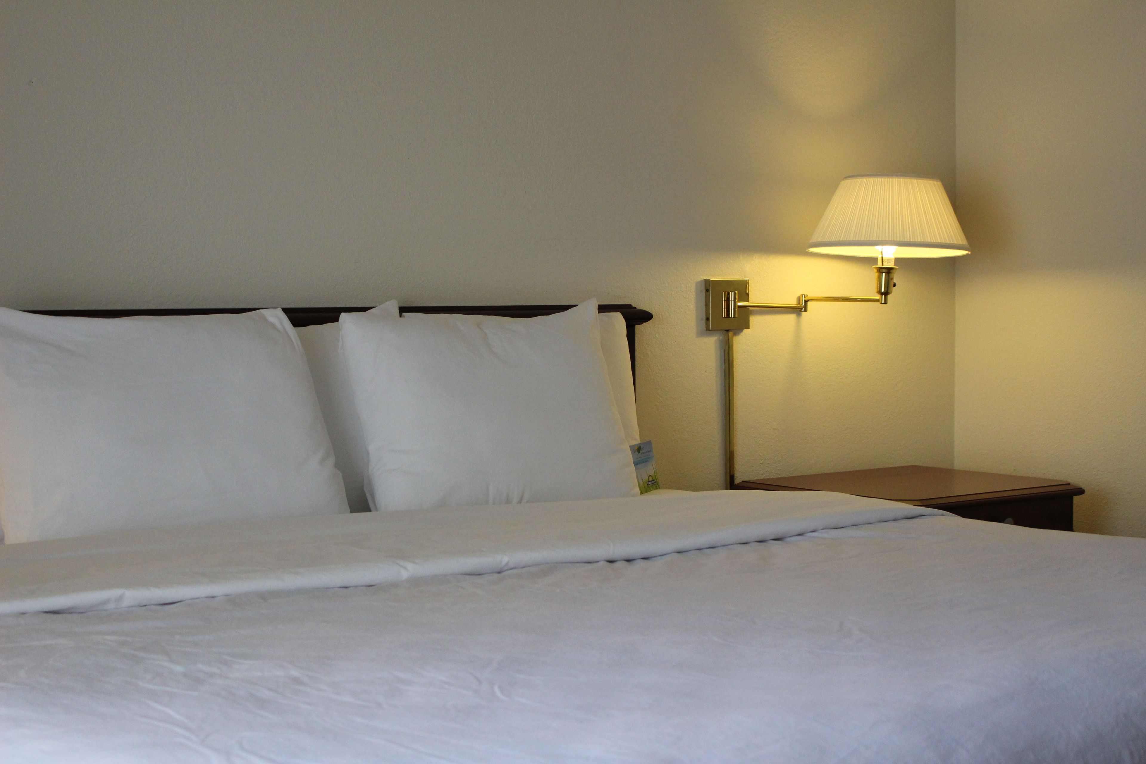 A neatly made bed with white linens, a bedside table with a lamp, and a wall-mounted light fixture.