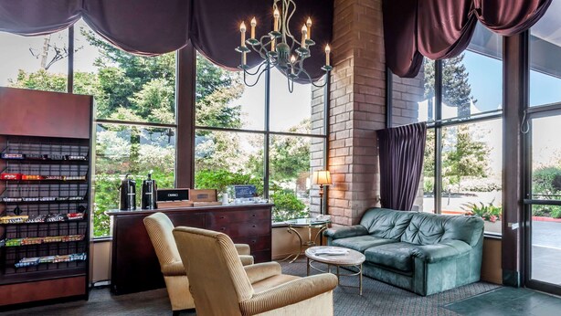 A hotel lobby with a large window, a chandelier, a sofa, a chair, a small table, and a bookshelf. - Days Inn & Suites by Wyndham Sunnyvale (Sunnyvale)