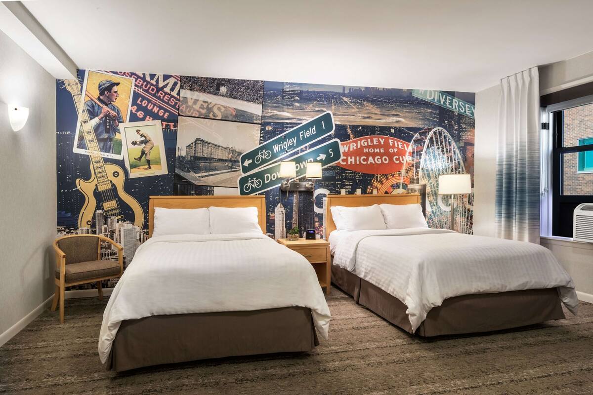 Une chambre d’hôtel avec deux lits, une fresque représentant un paysage urbain sur le mur et une vue sur la ville.