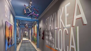 A hotel corridor with a blue carpet, a colorful ceiling light fixture, and walls with motivational phrases like "STAY LIKE A LOCAL". - Hotel Versey Chicago Lincoln Park (Chicago)