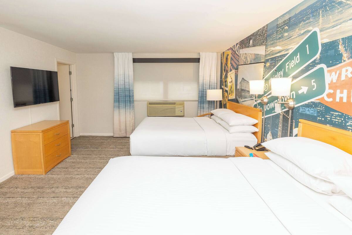 Une chambre d’hôtel avec deux lits, une télévision, une commode en bois et un mur orné de panneaux de signalisation.