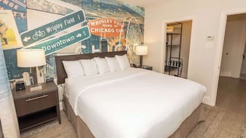 A hotel room with a large bed, a nightstand with a lamp, a wall mural, and a door leading to another room.