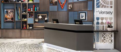 A hotel reception area with a modern design, featuring a reception desk, a wall with various memorabilia, and a patterned floor.
