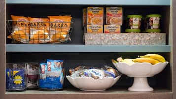 A pantry shelf with snacks, instant meals, and a bowl of bananas.