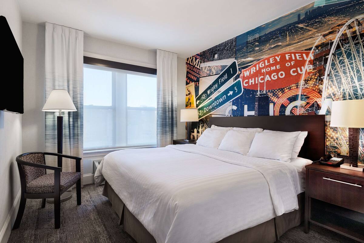 Une chambre d’hôtel avec un grand lit, une chaise, une table de chevet et un mur orné d’une fresque représentant l’équipe des Chicago Cubs.