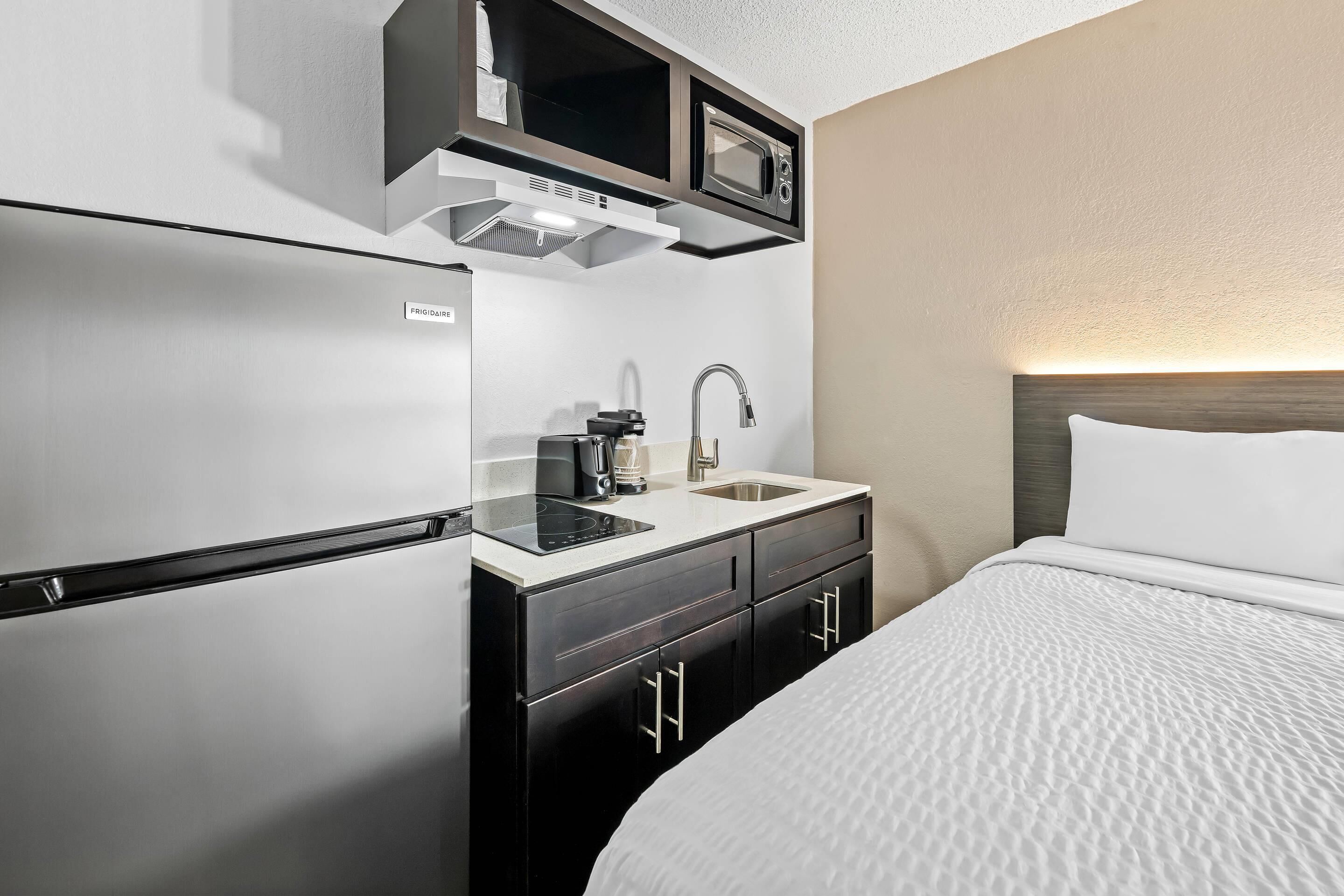 A compact hotel room with a kitchenette, including a refrigerator, microwave, and sink.