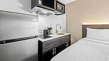 A compact hotel room with a kitchenette, including a refrigerator, microwave, and sink.