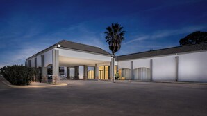 A modern building with a covered outdoor area, a palm tree, and a clear sky. - Suburban Studios Pecos (Pecos)