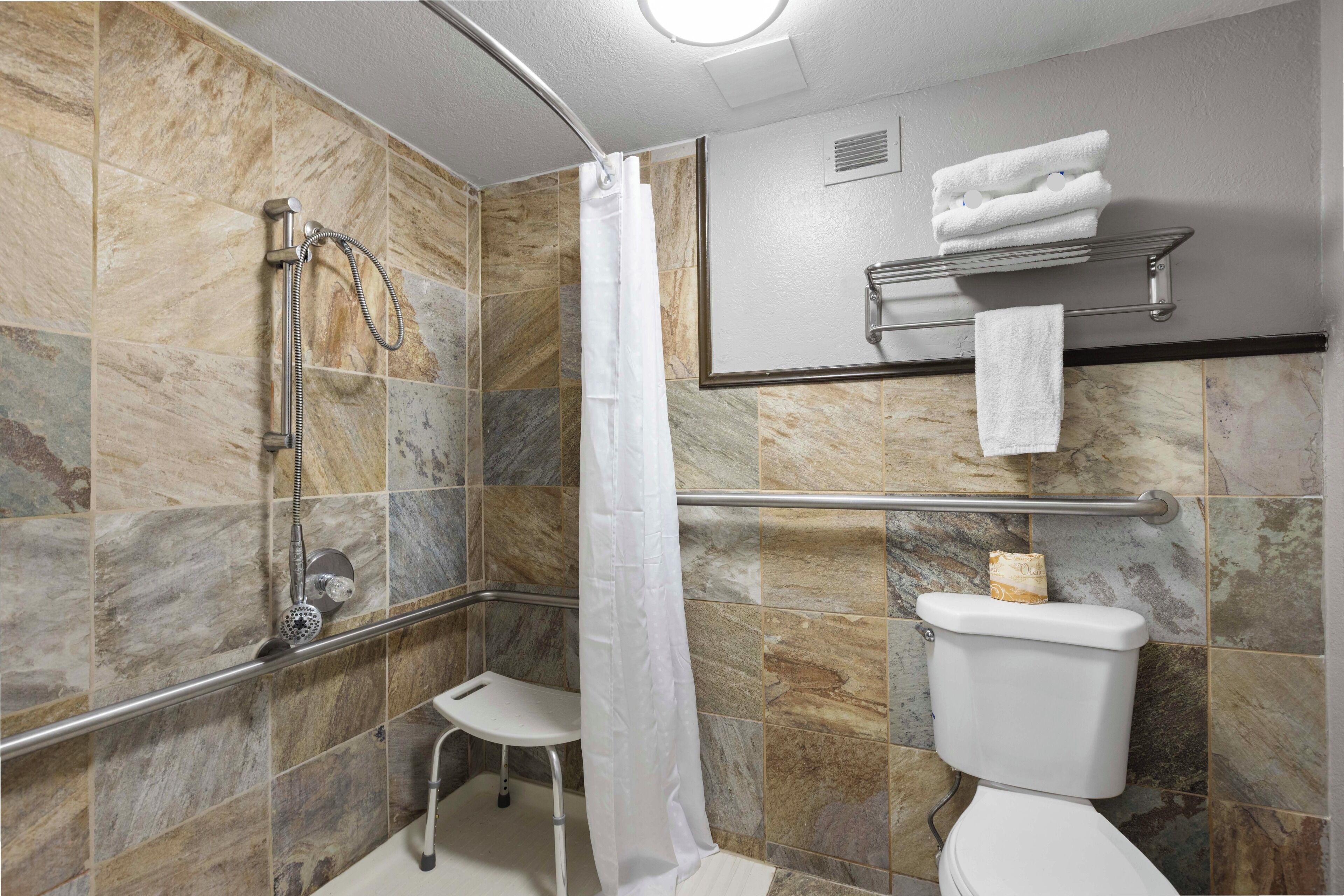 A bathroom with a shower, toilet, and a small white bench.
