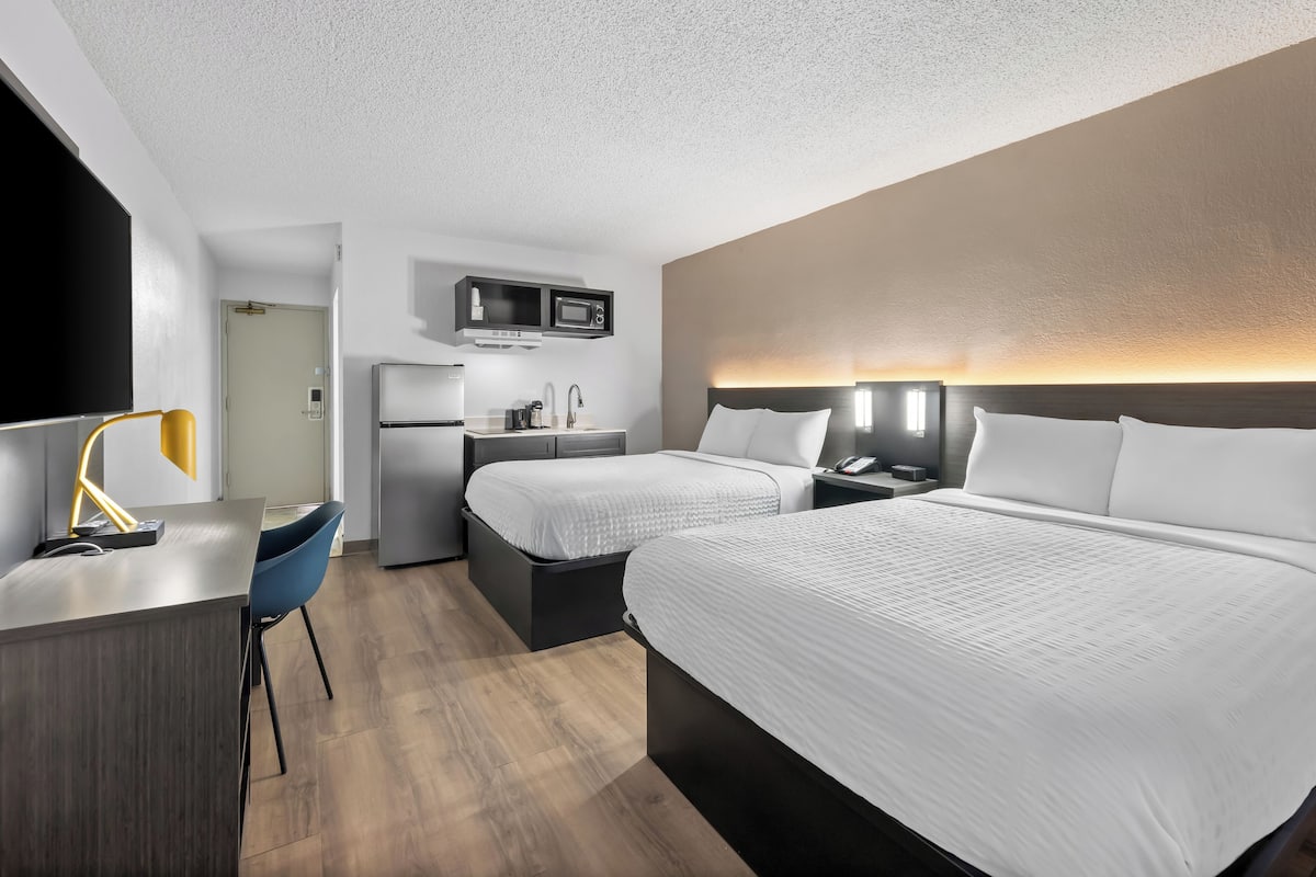Ein modernes Hotelzimmer mit zwei Betten, einem Schreibtisch, einem Stuhl, einer Mikrowelle und einem Kühlschrank.