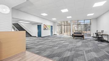 Una oficina amplia con suelo alfombrado, una escalera, un mostrador de recepción y ventanas grandes.