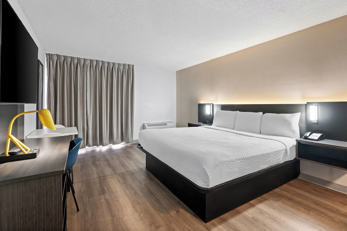 Ein modernes Hotelzimmer mit einem großen Bett, Nachttischen, einem Schreibtisch mit Stuhl und einem Fernseher.