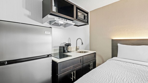 A compact hotel room with a kitchenette, including a refrigerator, microwave, and sink. - Suburban Studios Pecos (Pecos)