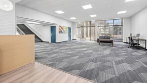 A spacious office area with a carpeted floor, a wooden reception desk, a staircase, and large windows. - Suburban Studios Pecos (Pecos)
