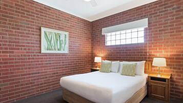 A hotel room with a brick wall, a large bed with white bedding, two bedside tables with lamps, and a ceiling fan.