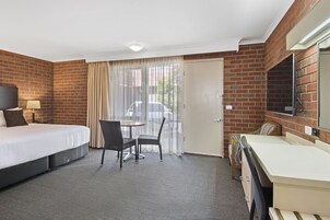 Habitación de hotel con cama, escritorio, silla, televisión y puerta corrediza al exterior.