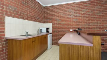 A compact kitchen with a brick wall, wooden cabinets, a white countertop, a sink, a microwave, and a refrigerator.