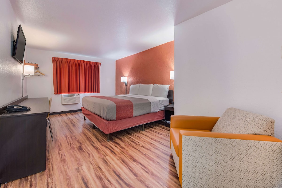 A hotel room with a bed, a desk, a chair, and a television mounted on the wall.