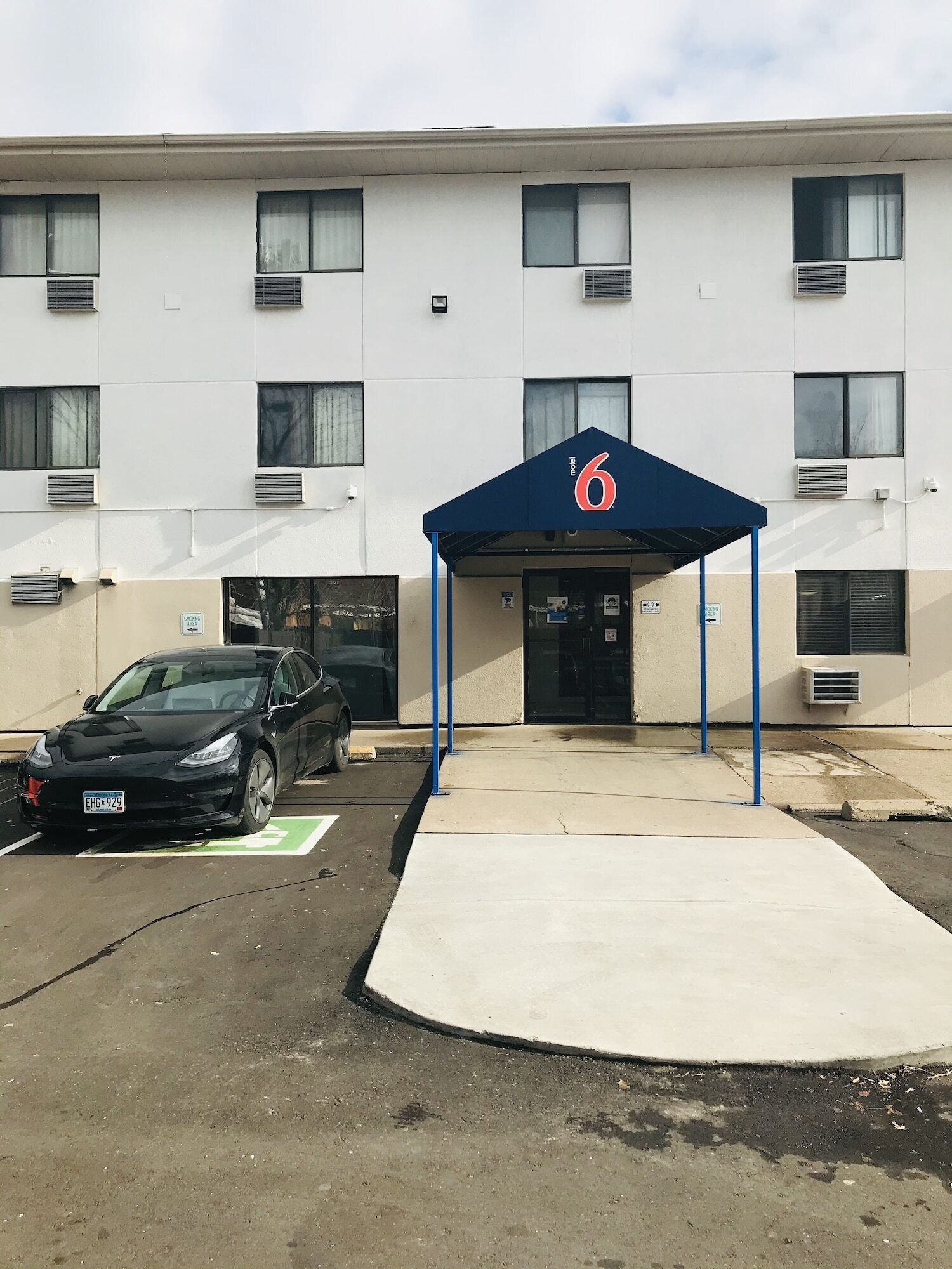 Edifici amb tendal blau que mostra el número 6, indicant a un motel o hotel. Hi ha una zona de pàrquing amb estació de càrrega per Tesla.
