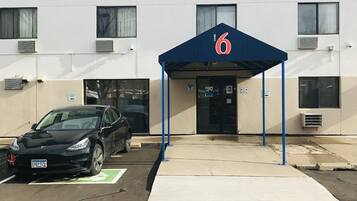 Edifici amb tendal blau que mostra el número 6, indicant a un motel o hotel. Hi ha una zona de pàrquing amb estació de càrrega per Tesla.