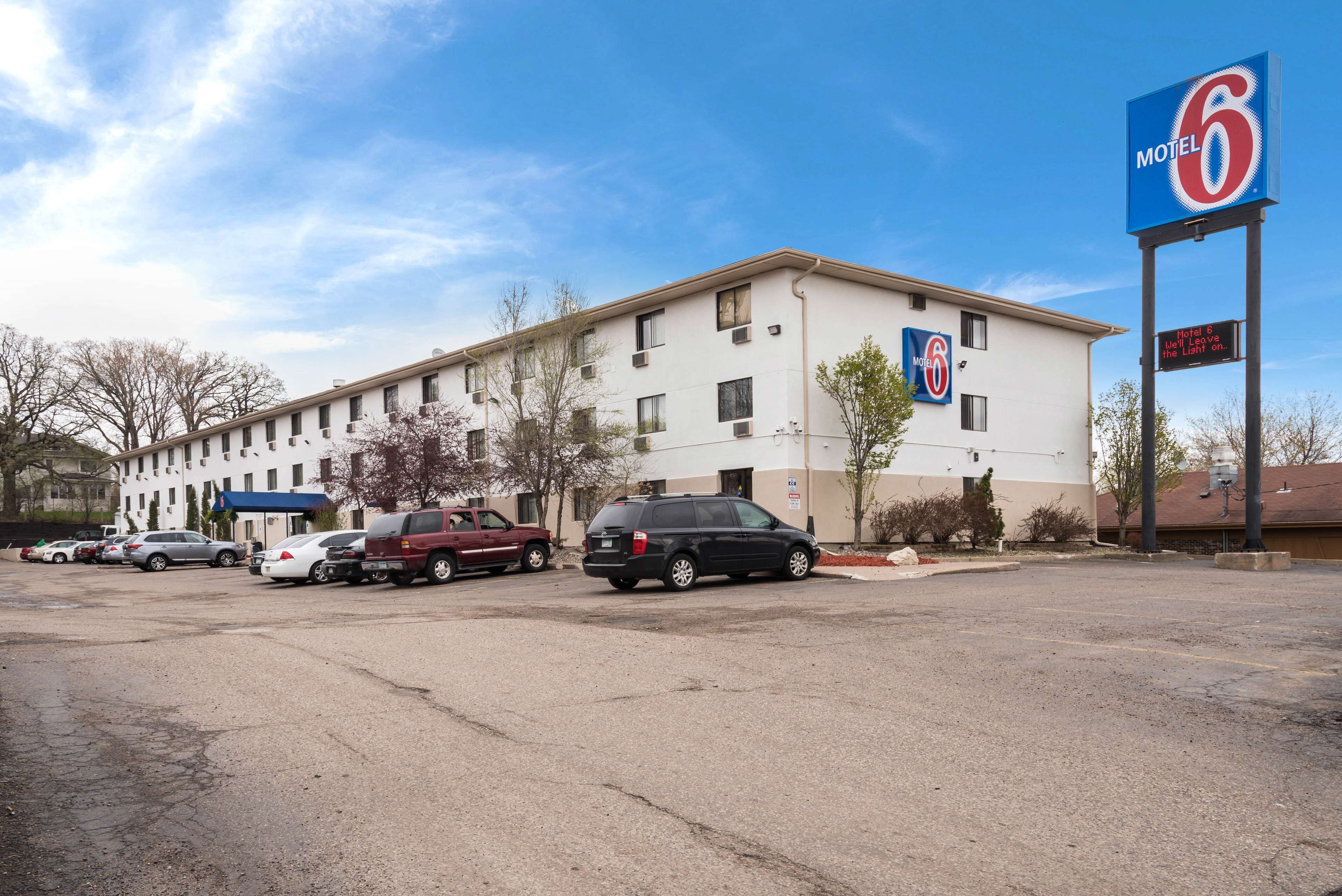A motel with a large sign, a parking lot, and several cars parked in front.