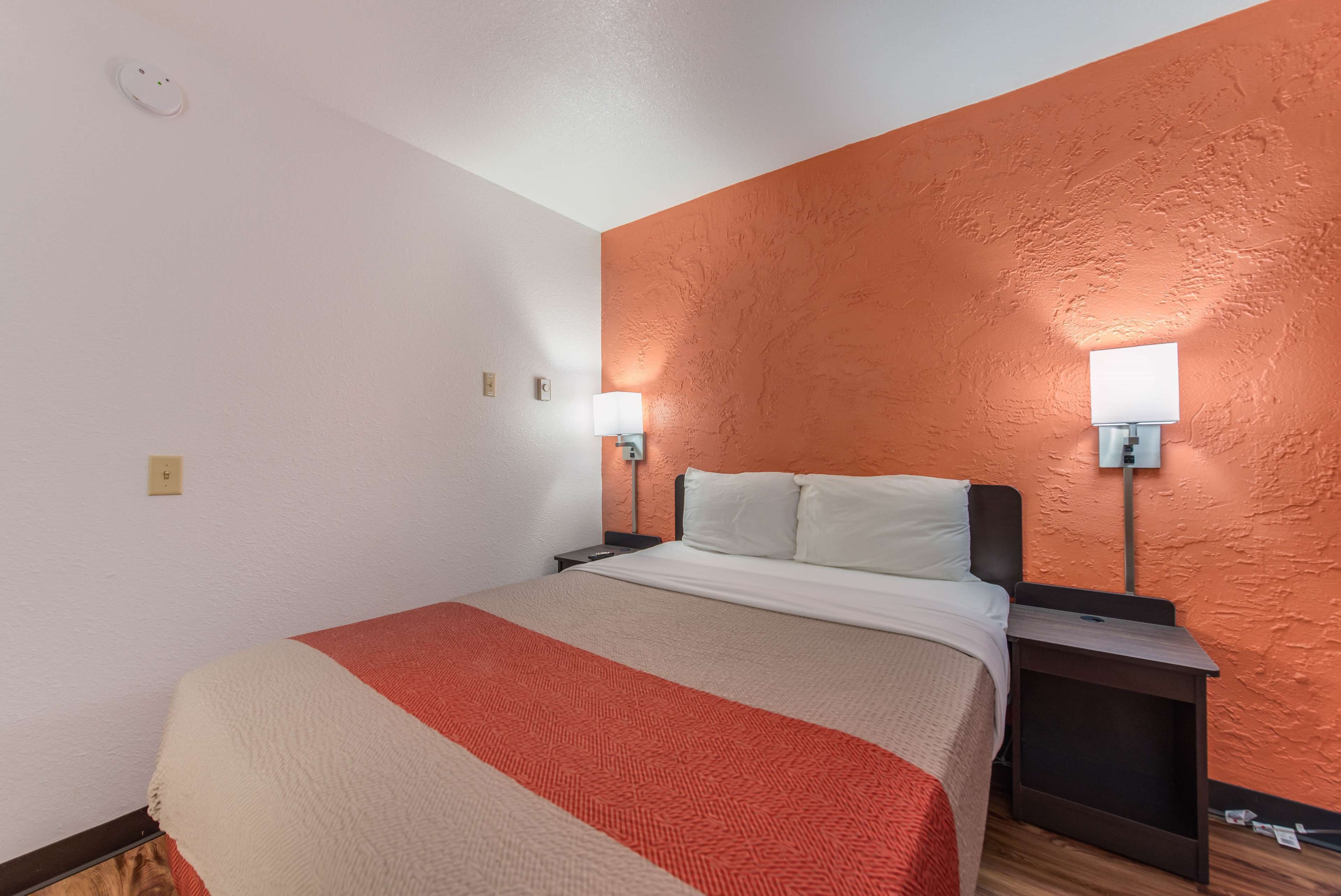 A hotel room with a bed, two bedside tables, a nightstand, and two wall-mounted lamps.