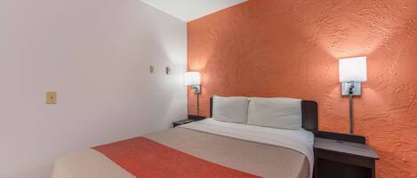 A hotel room with a bed, two bedside tables, a nightstand, and two wall-mounted lamps.
