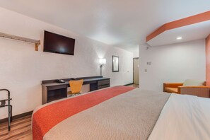 Habitación de hotel con cama, escritorio, silla, televisor montado en la pared y puerta que da a otra habitación.