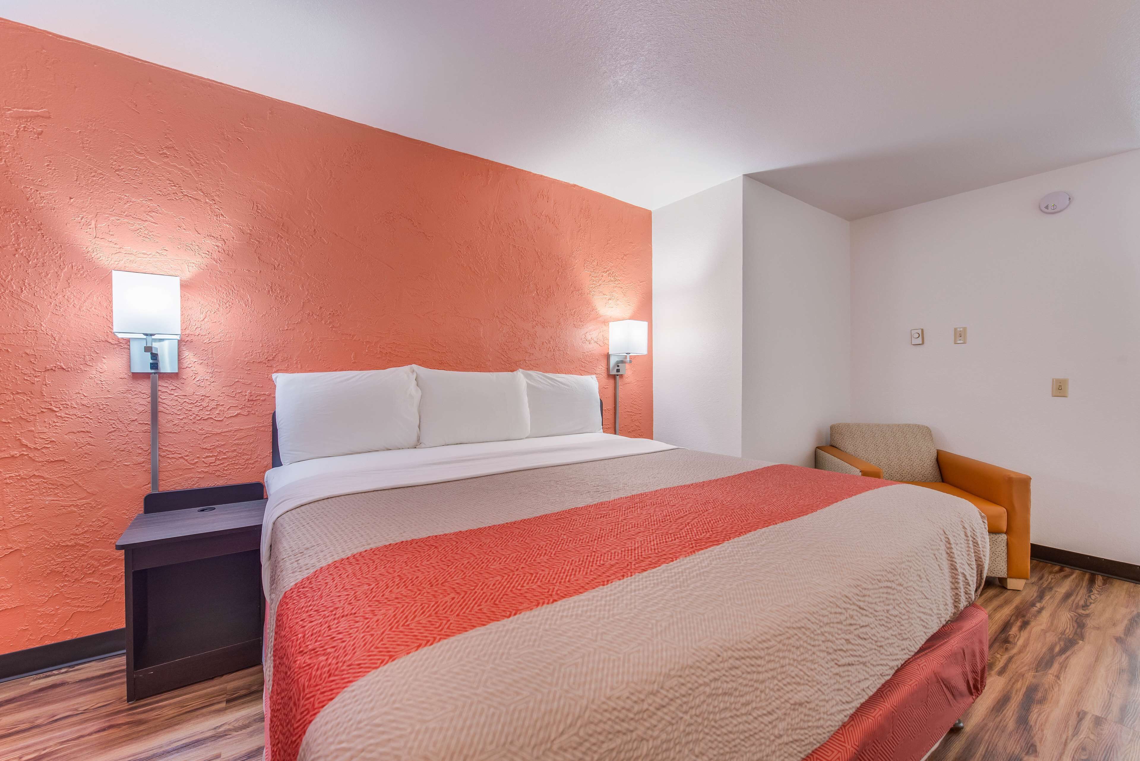 A hotel room with a large bed, two bedside lamps, a nightstand, and a chair.