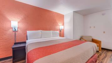 A hotel room with a large bed, two bedside lamps, a nightstand, and a chair.