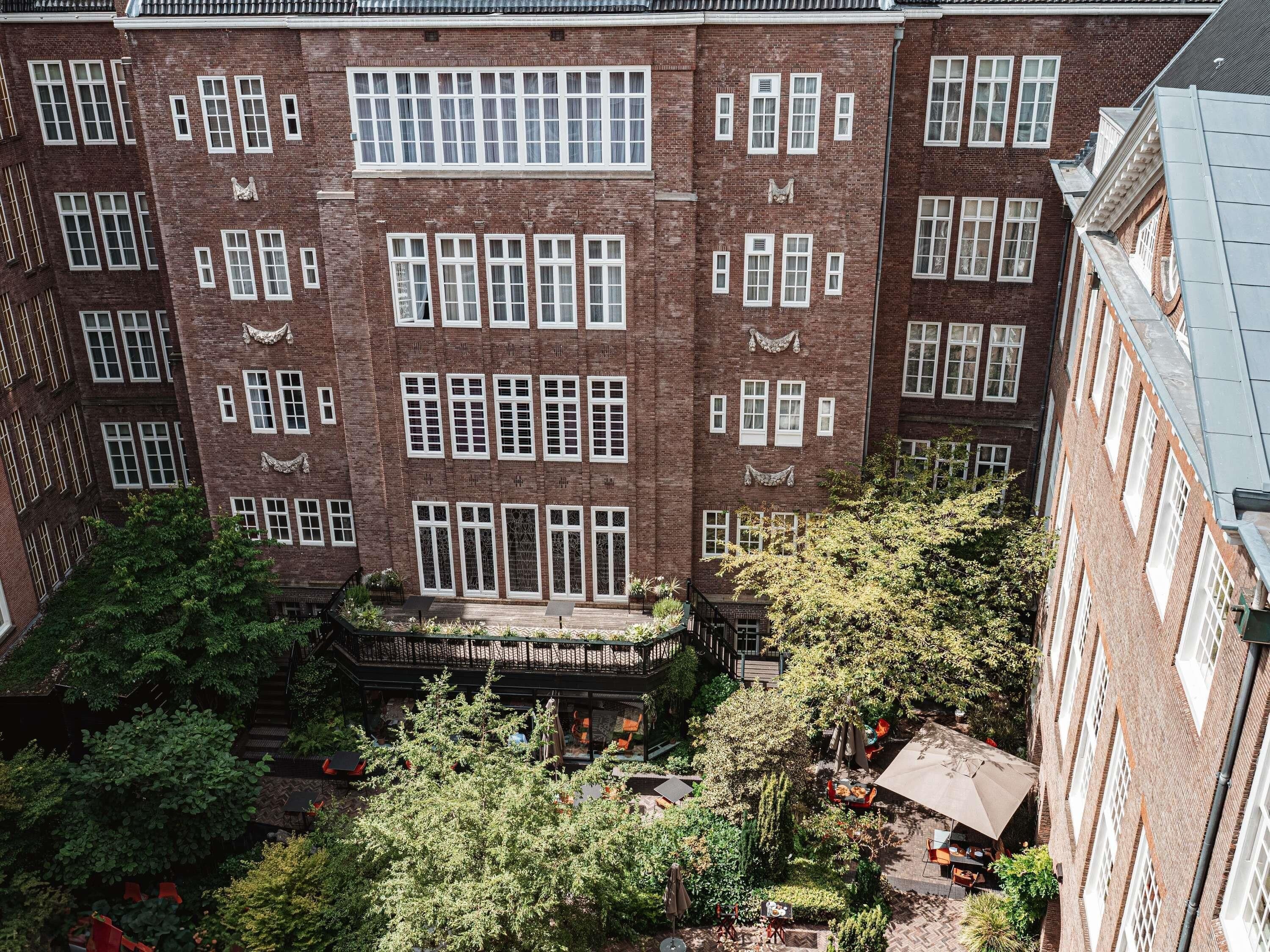Un edificio de ladrillo de varios pisos con ventanas uniformes y un patio central con árboles y mobiliario exterior.
