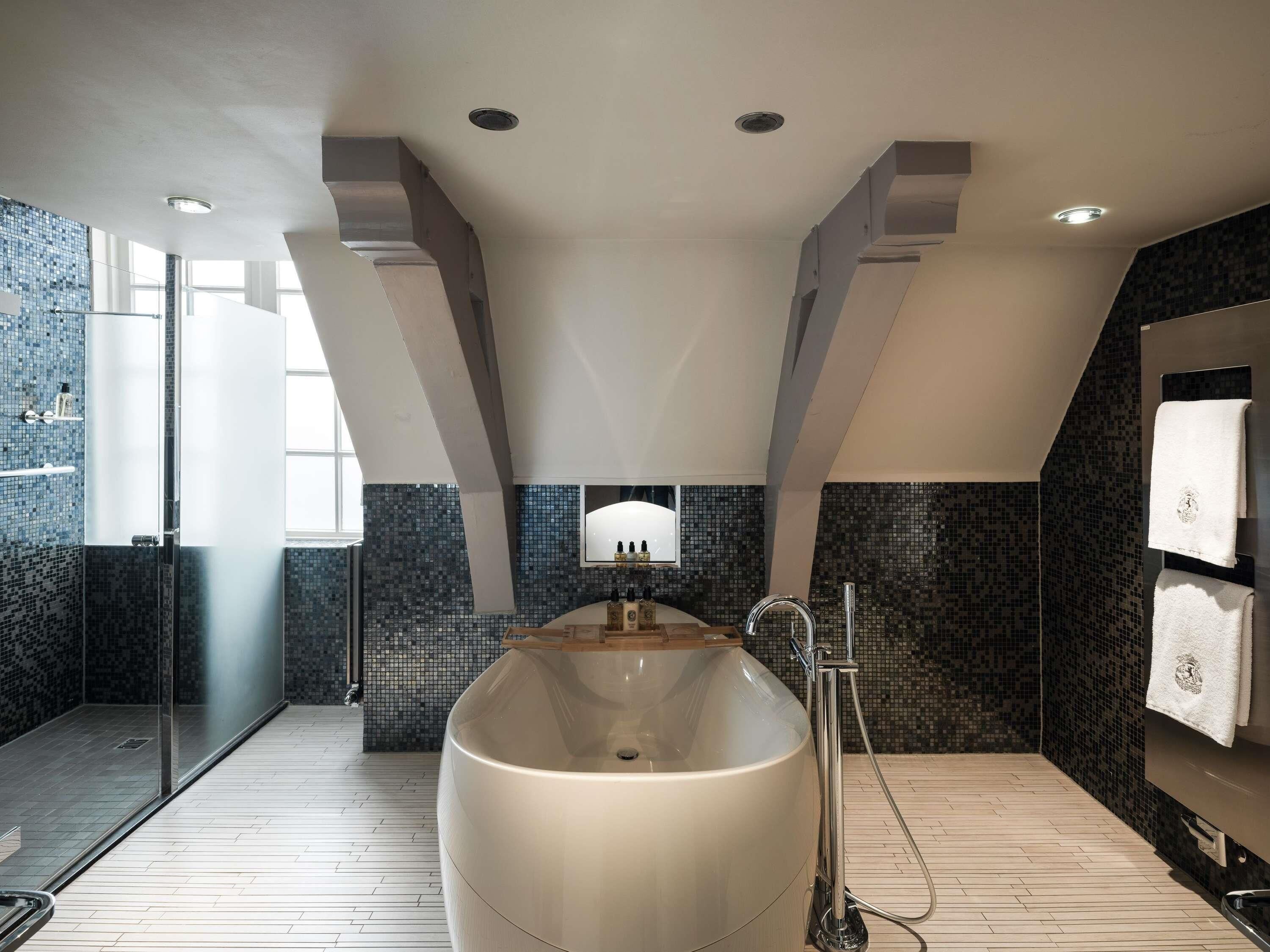 A modern bathroom with a large freestanding bathtub, a glass shower enclosure, and a tiled mosaic wall.