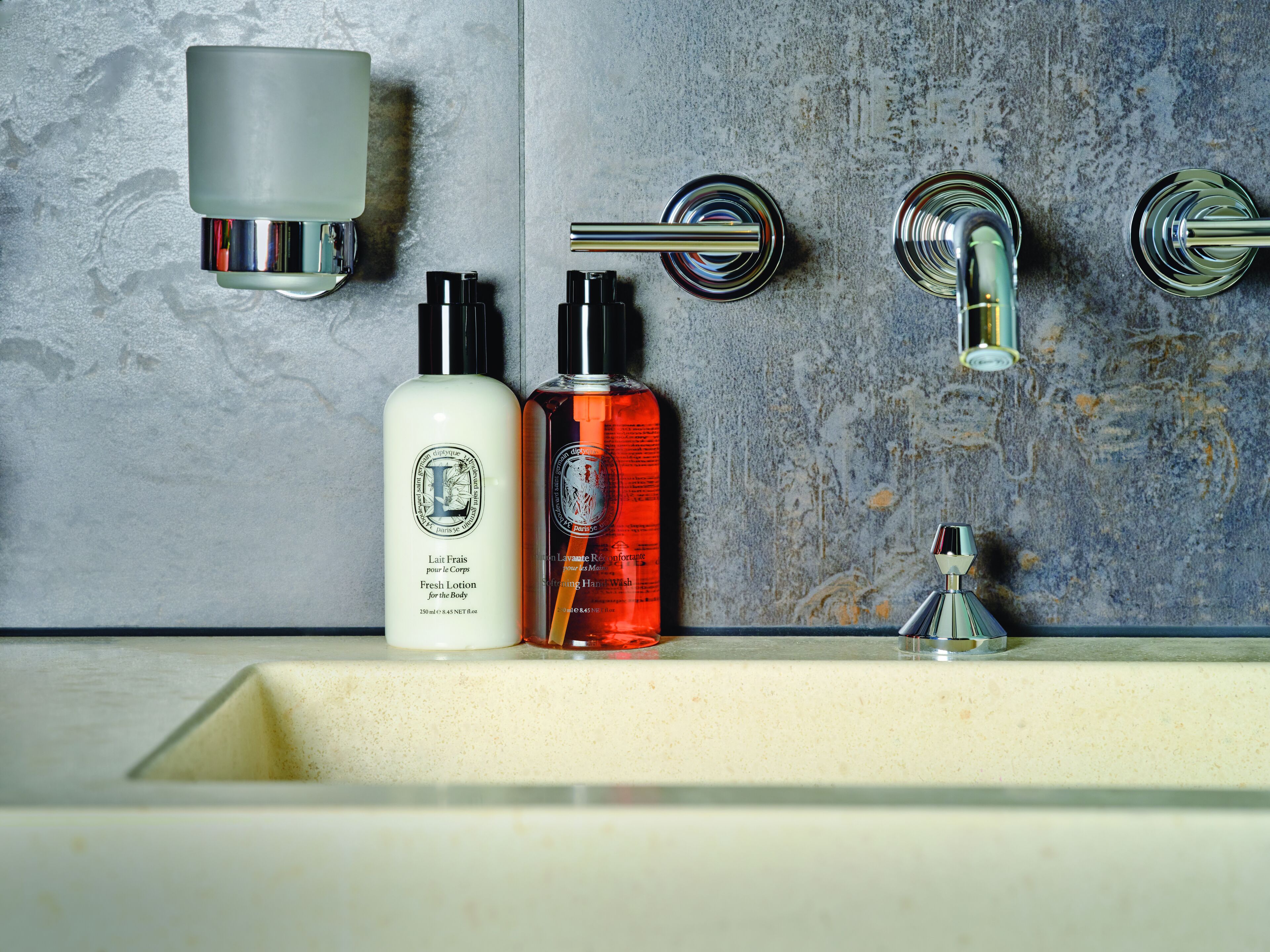 A bathroom with a marble wall, a sink, and two bottles of lotion.