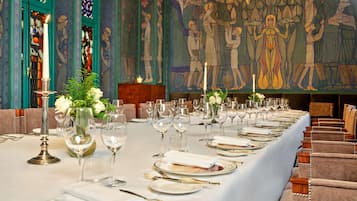A long dining table set for a meal in a room with a mural and stained glass windows.
