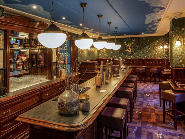 A bar area with a long counter, multiple stools, and a decorative ceiling.