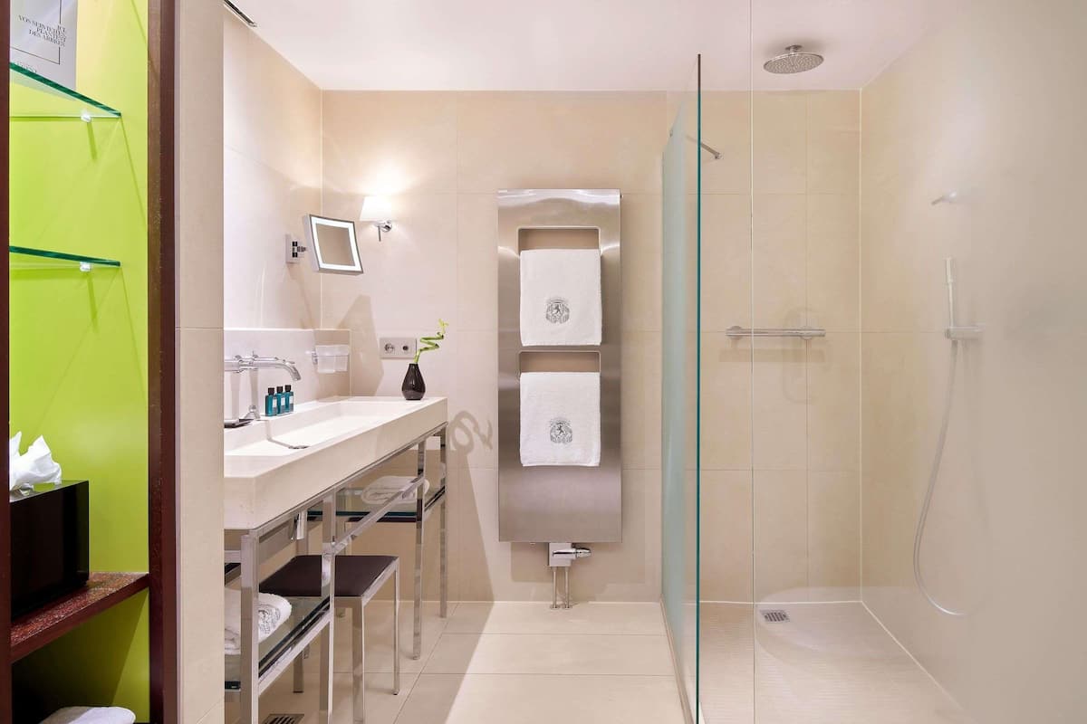 A modern bathroom with a glass shower enclosure, a vanity with a mirror, and a shelf with towels.
