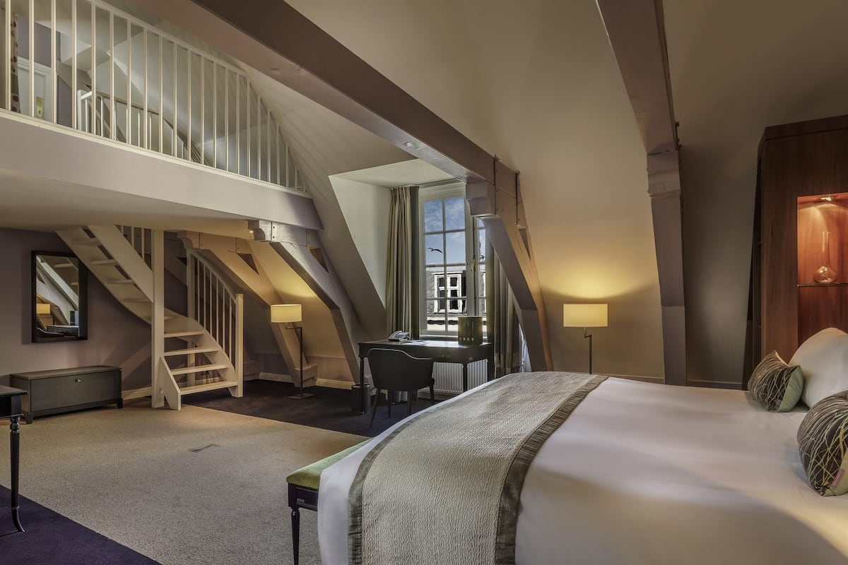 A hotel room with a bed, desk, chair, lamp, and a staircase leading to an upper level.