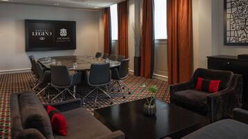A conference room with a large table, chairs, a sofa, and a TV screen displaying 'SOFITEL LEGEND THE GRAND AMSTERDAM 1578'.