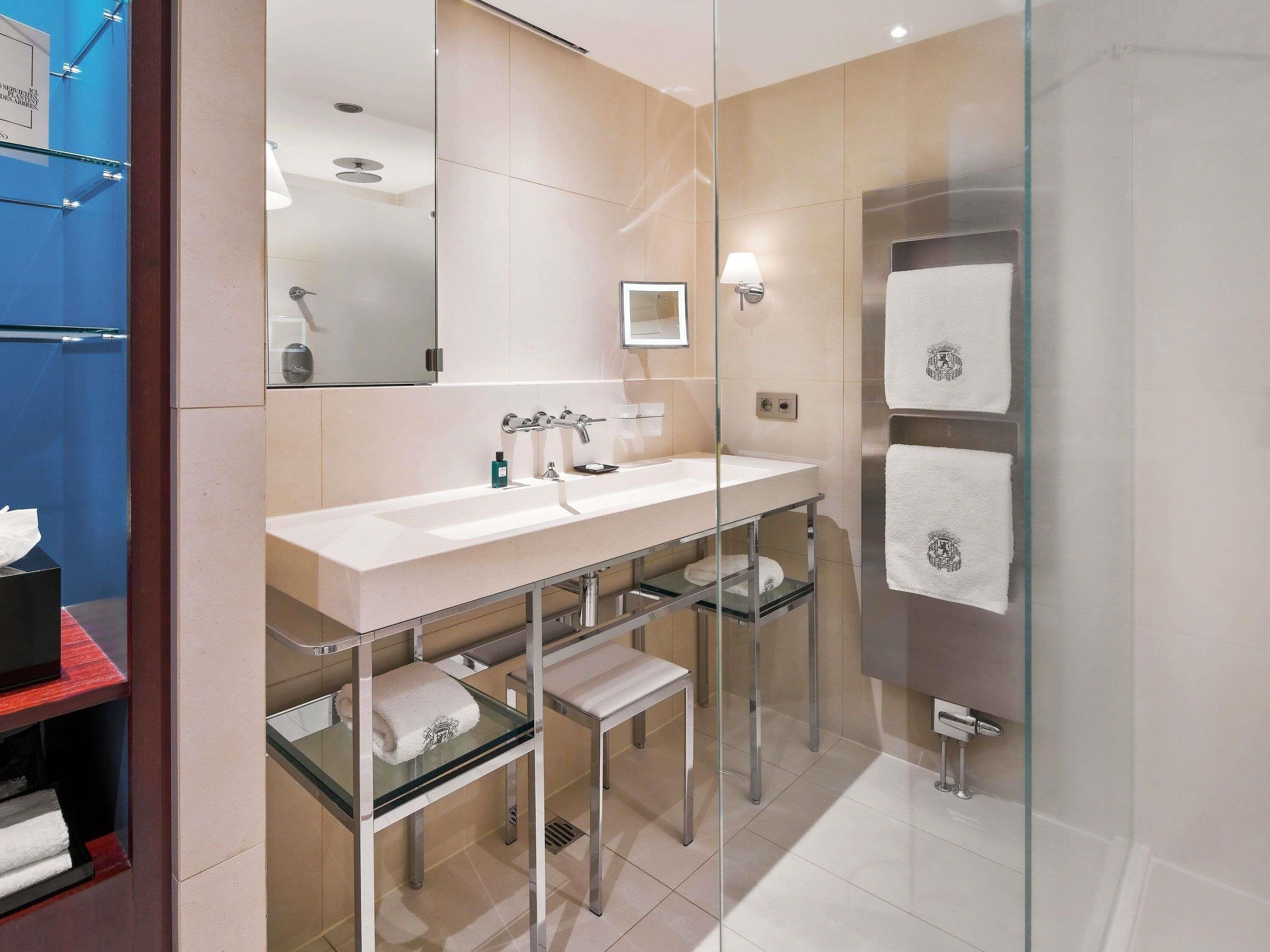 Un bany modern amb plat de dutxa envoltat de vidre, un lavabo doble i un moble amb mirall.