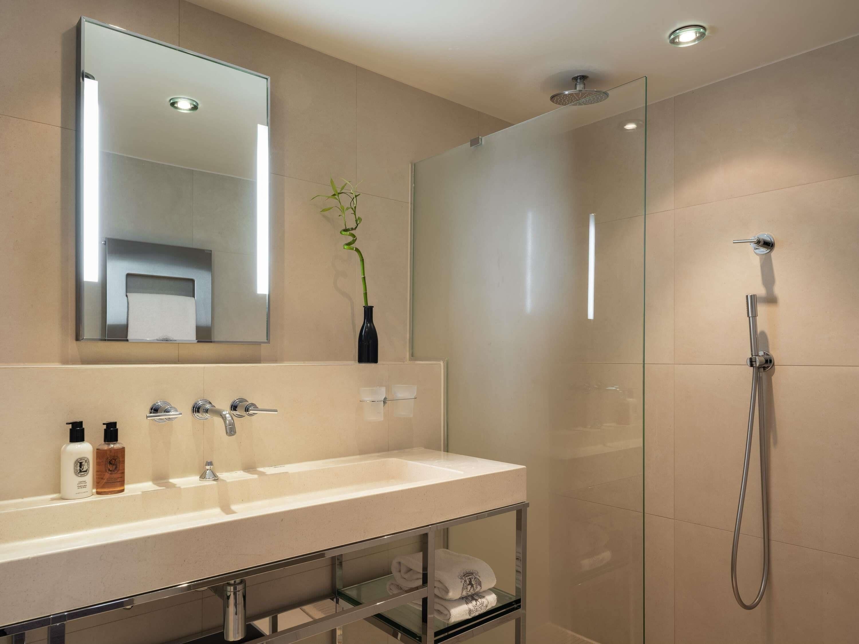 A modern bathroom with a large mirror, a glass shower enclosure, and a vanity with a sink and towel rack.
