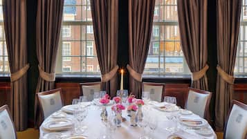 A dining room with a round table set for six, flanked by curtains and a window with a view of buildings.