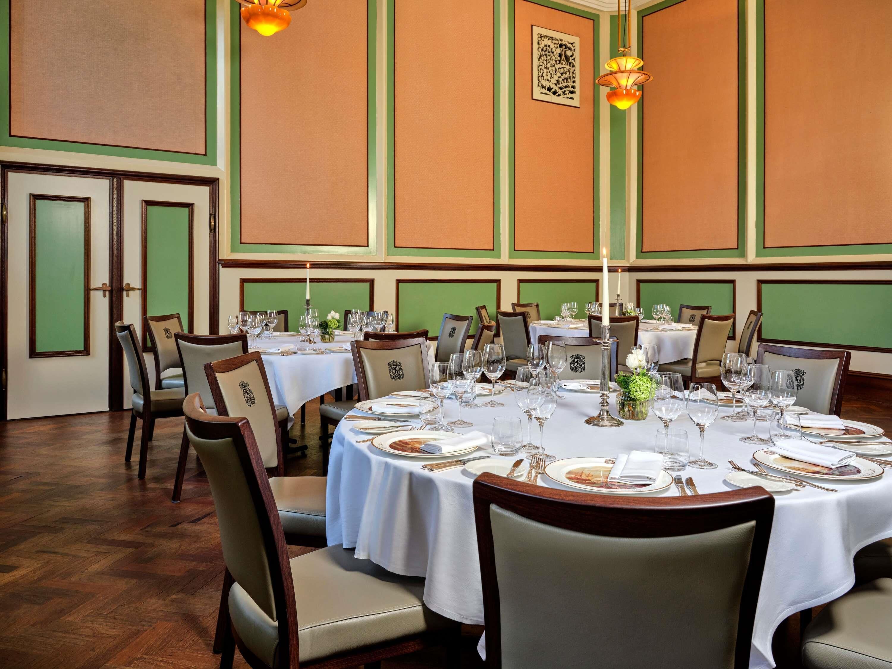 A dining area with round tables set for service, chairs, and a large candle centerpiece.