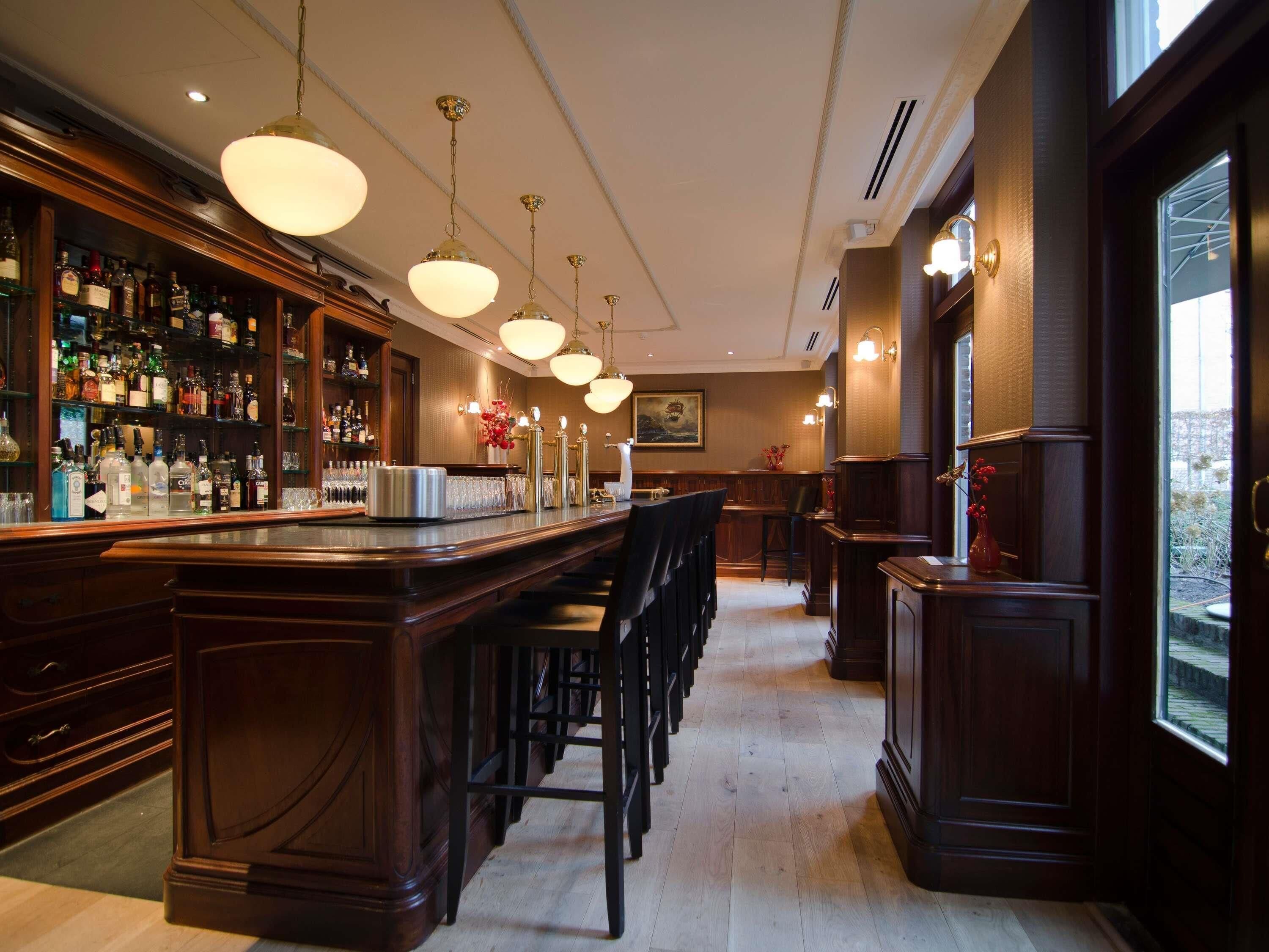 A bar area with a long counter, multiple hanging light fixtures, and a variety of bottles and glasses on shelves.