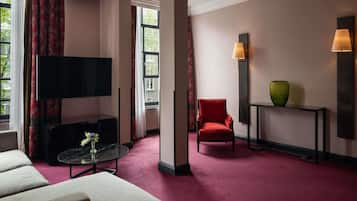 Habitación de hotel con televisor de pantalla plana, un sillón rojo, una mesita con un florero y una consola con otro florero.