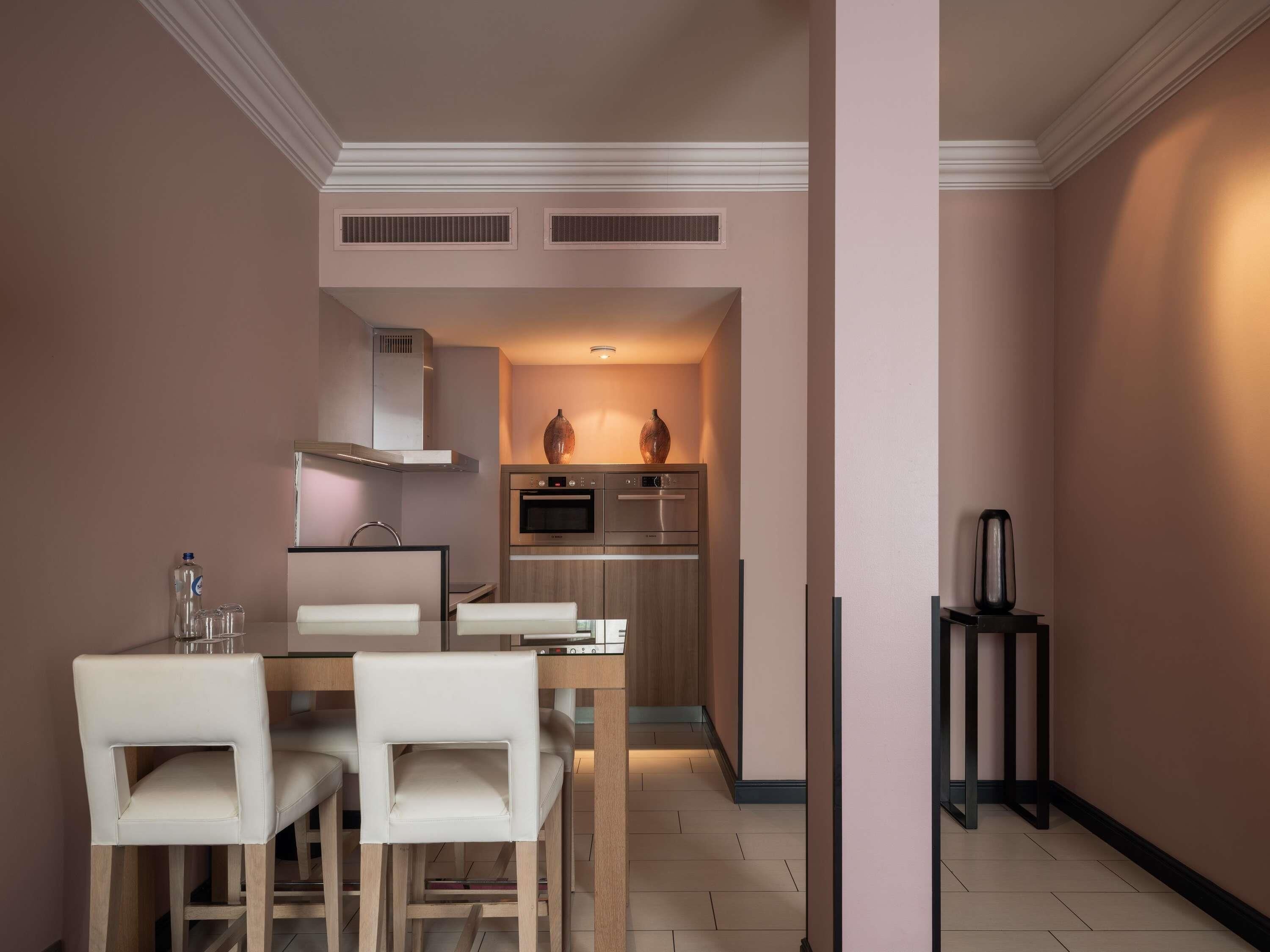 A modern kitchen with a dining area, featuring a table with chairs, a built-in oven, and a coffee machine.