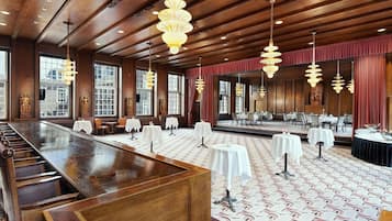 A spacious hotel lobby with a long reception counter, multiple tables, and elegant chandeliers.